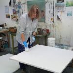 Photograph of British artist Hilary Barry priming canvases in her Kessingland studio.